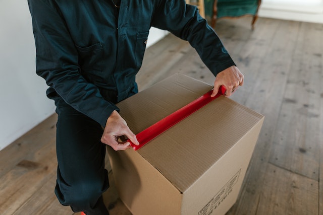 someone closing a cardboard box with red tape
